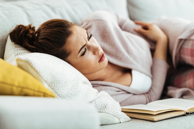 Jeune femme ayant des maux d'estomac en position allongée sur un canapé dans le salon