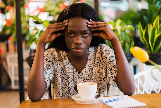 Jeune femme ayant des maux de tête tout en travaillant sur un ordinateur portable au café