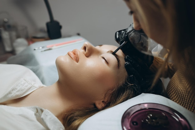 Jeune femme ayant une procédure professionnelle de correction des sourcils dans un salon de beauté