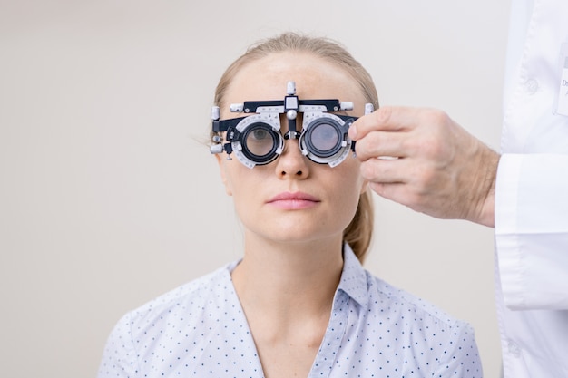 Jeune femme ayant sa vision des yeux examinée tout en regardant à travers une lentille optométrique dans les cliniques