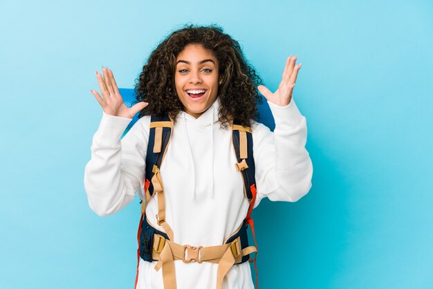 Jeune femme backpacker afro-américaine recevant une agréable surprise, excité et levant les mains.