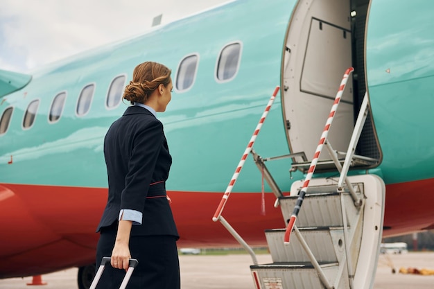 La jeune femme avec le bagage est dehors près de l'avion