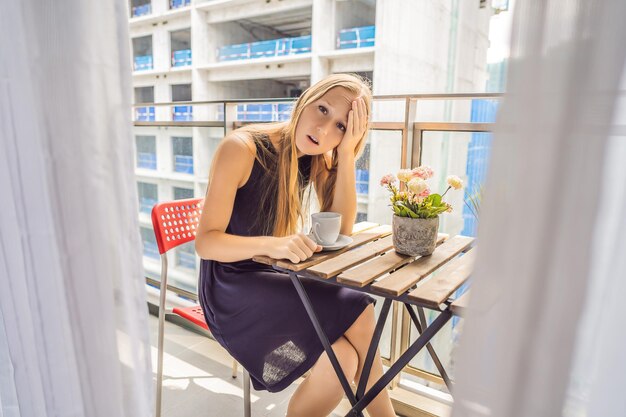 Jeune femme sur le balcon agacée par les travaux de construction à l'extérieur Concept de bruit Pollution de l'air par la poussière de construction