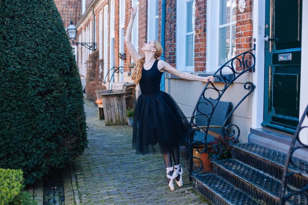 Jeune femme ballerine aux cheveux rouges en costume de ballet et chaussures de pointe est dans une belle pose dansant sur la rue.