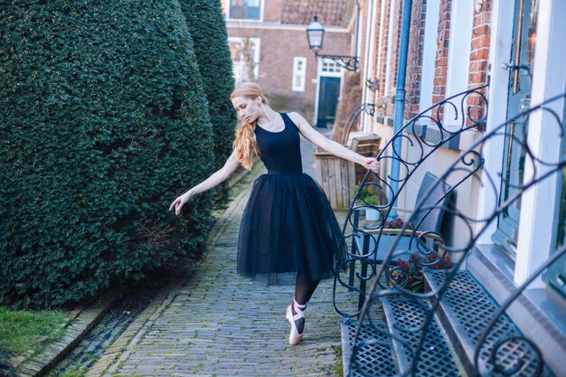 Jeune femme ballerine aux cheveux rouges en costume de ballet et chaussures de pointe est dans une belle pose dansant sur la rue.