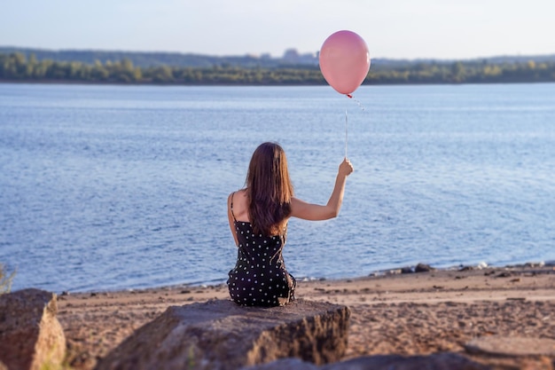 La jeune femme avec un ballon solitaire s'assied et regarde la rivière