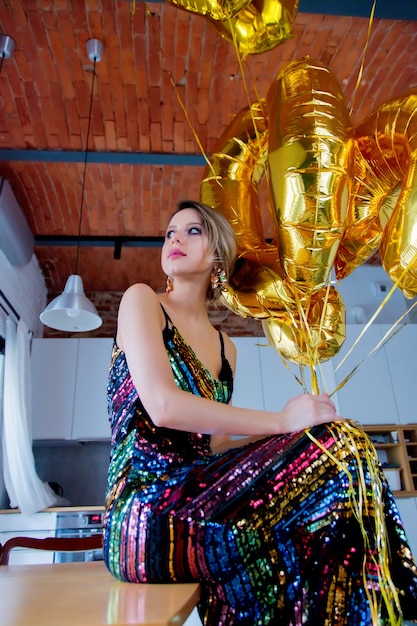 Jeune femme avec des ballons dorés pour son anniversaire de trente ans. La personne est en robe et coiffure vintage 80e. À la maison
