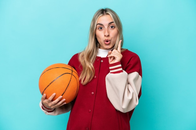 Jeune femme de basket-ball caucasienne isolée sur fond bleu ayant l'intention de réaliser la solution tout en levant un doigt