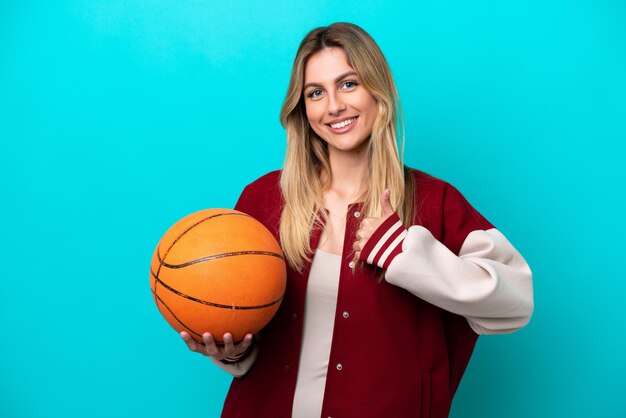 Jeune femme de basket-ball caucasienne isolée sur fond bleu donnant un geste du pouce levé