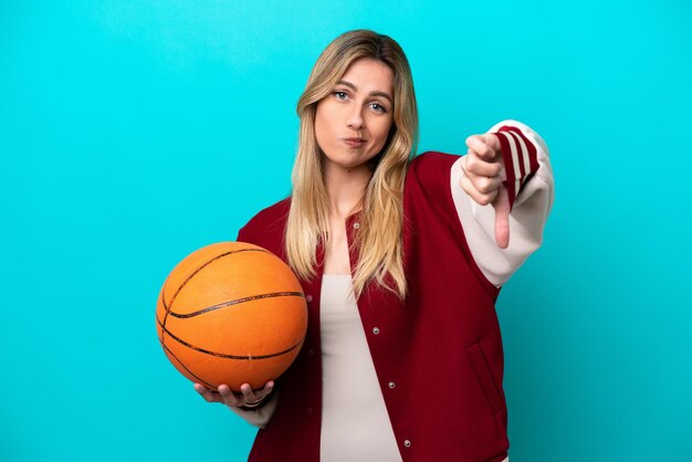 Jeune femme de basket-ball caucasienne isolée sur fond bleu montrant le pouce vers le bas avec une expression négative