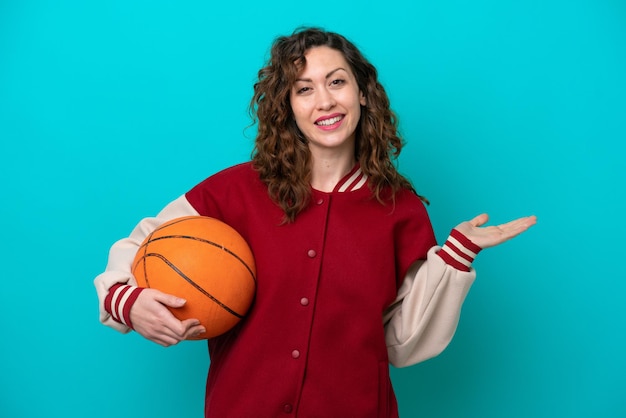 Jeune femme de basket-ball caucasienne isolée sur fond bleu tendant les mains sur le côté pour inviter à venir