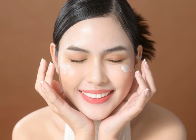 Une jeune femme avec un beau visage tient de la crème à l'aide de la crème de son concept de soins de la peau de beauté du visage