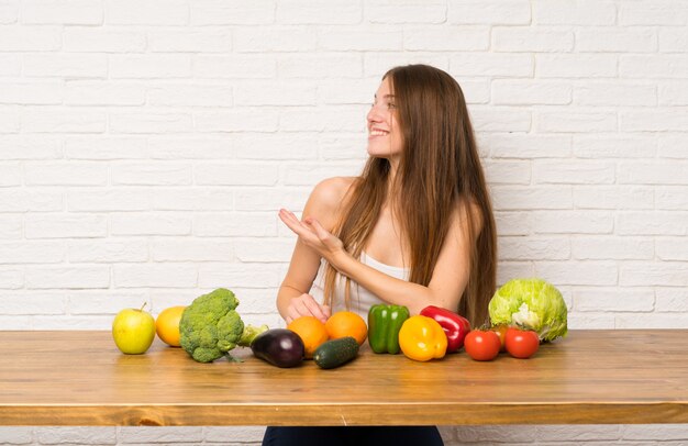 Jeune femme avec beaucoup de légumes s'étendant les mains sur le côté pour avoir invité à venir