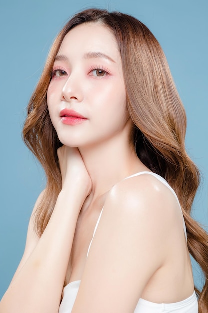 Jeune femme de beauté asiatique cheveux longs bouclés avec un style de maquillage coréen sur le visage et une peau propre parfaite sur fond bleu isolé Traitement du visage Chirurgie plastique cosmétologie