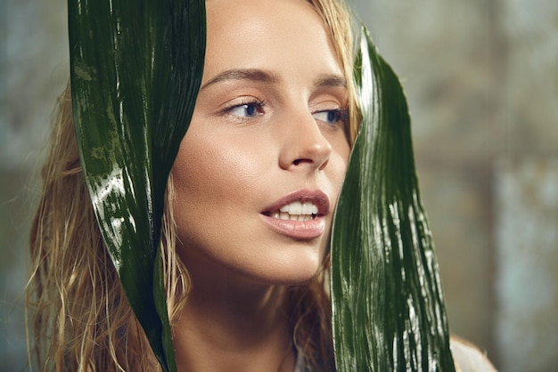 Jeune femme de beauté avec une peau parfaite tient des pétales tropicaux près du visage en gros plan