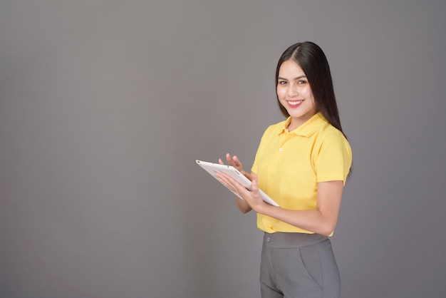 Jeune femme belle confiante portant une chemise jaune tient une tablette sur studio gris