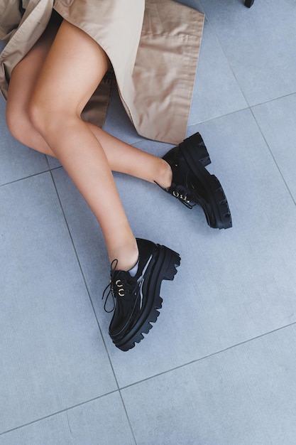 Une jeune femme avec de belles jambes minces dans des chaussures en cuir noir à la mode est assise sur une chaise dans le studio