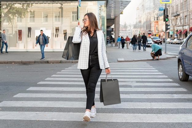 Photo une jeune femme bien habillée tient un sac en papier noir avec un espace pour copier du texte ou un dessin une fille traverse la route au passage pour piétons