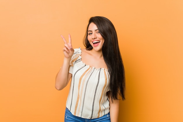 Jeune femme bien roulée montrant le signe de la victoire et souriant largement.