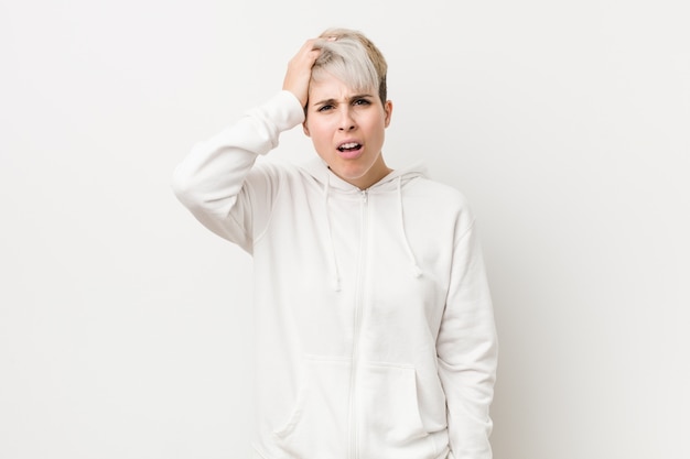 Jeune femme bien roulée portant un chandail à capuchon blanc fatigué et très somnolent en gardant la main sur la tête.