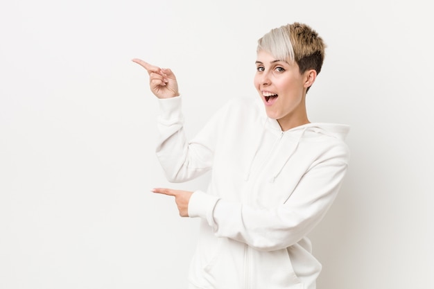 Jeune femme bien roulée portant un sweat à capuche blanc excité pointant avec les index loin.