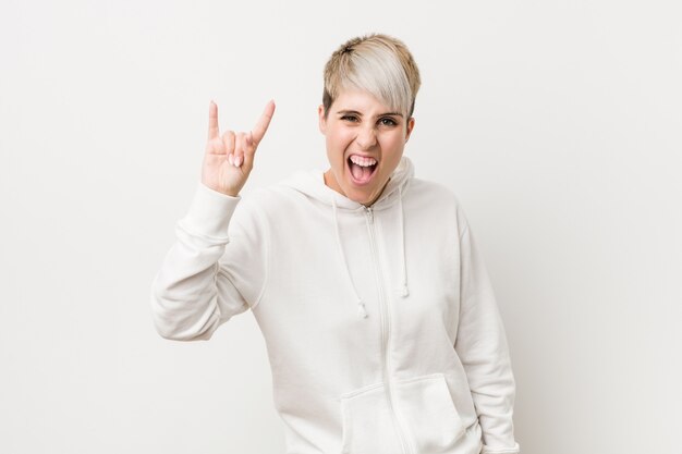 Jeune femme bien roulée portant un sweat à capuche blanc montrant un geste de cornes comme concept de révolution.