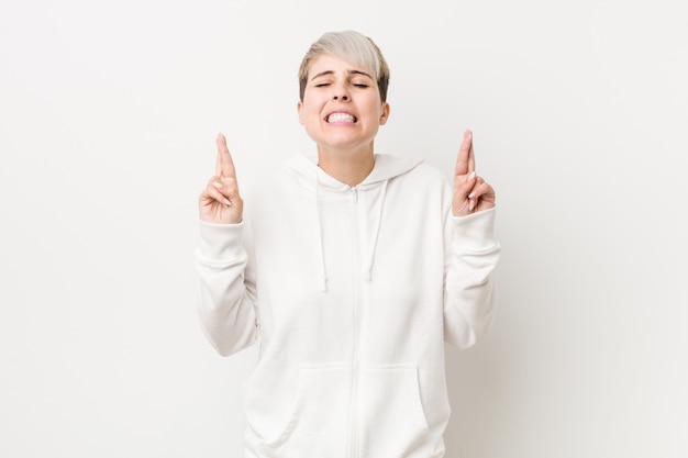 Jeune femme bien roulée portant un sweat à capuche blanc qui se croise les doigts pour avoir de la chance