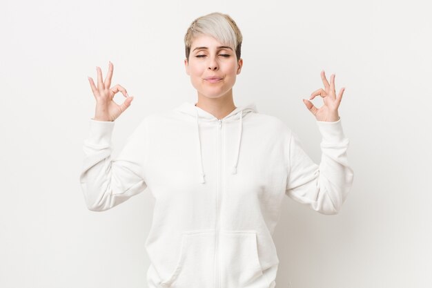 Jeune femme bien roulée portant un sweat à capuche blanc se détend après une dure journée de travail, elle pratique le yoga.