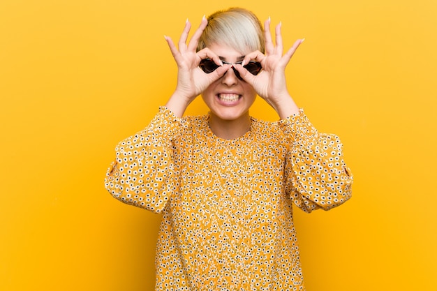 Jeune femme bien roulée portant un vêtement floral d'été montrant un signe correct sur les yeux