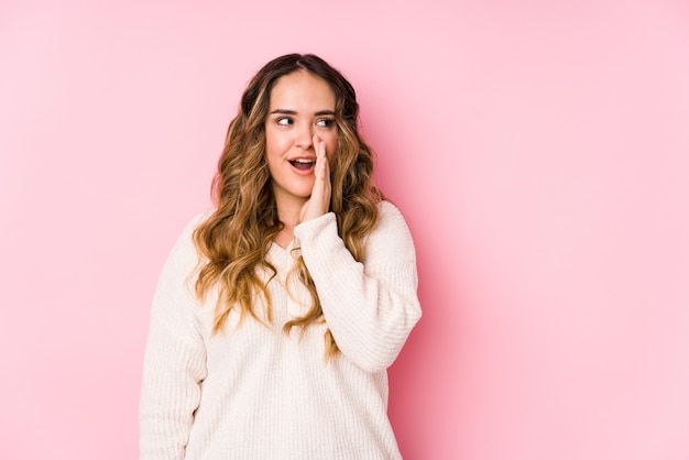 Jeune femme bien roulée posant dans un mur rose isolé dit une nouvelle de freinage chaude secrète et regardant de côté