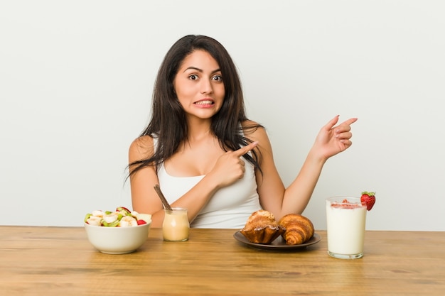 Jeune femme bien roulée prenant un petit déjeuner choqué pointant avec l'index vers un espace de copie.