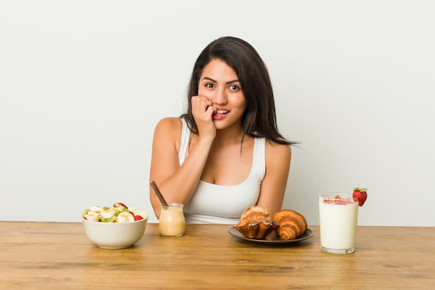 Jeune femme bien roulée prenant un petit déjeuner se ronger les ongles, nerveuse et très anxieuse.