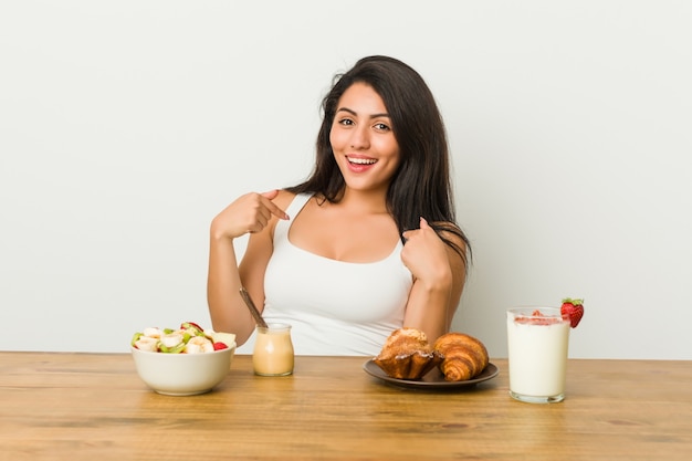 Jeune Femme Bien Roulée Prenant Un Petit Déjeuner Surpris En Pointant Avec Le Doigt, Souriant Largement.