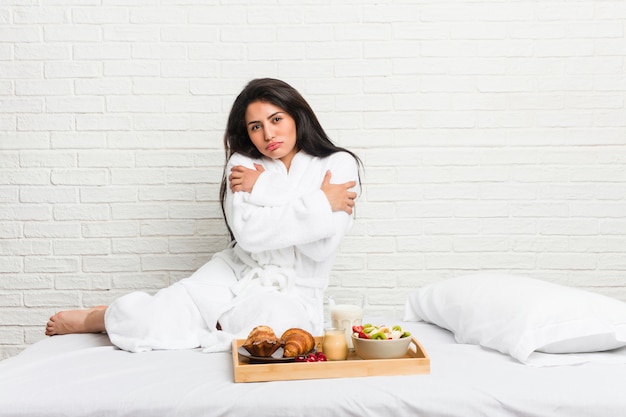 Jeune femme bien roulée prenant son petit déjeuner sur le lit, devenant froide en raison d'une température basse ou d'une maladie.