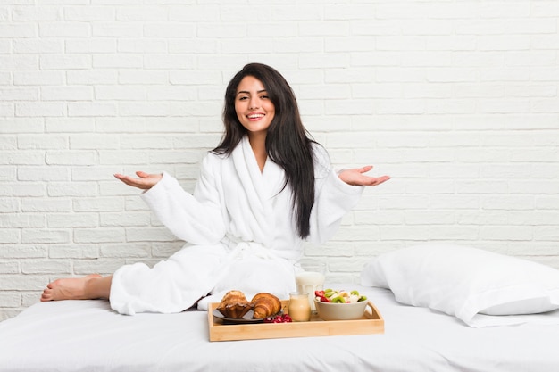 Jeune femme bien roulée prenant son petit déjeuner sur le lit montrant une expression bienvenue.