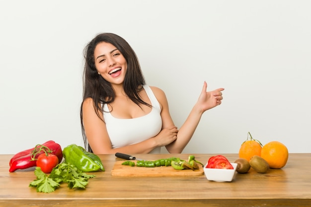 Jeune femme bien roulée préparer un repas sain souriant joyeusement pointant avec l'index loin.