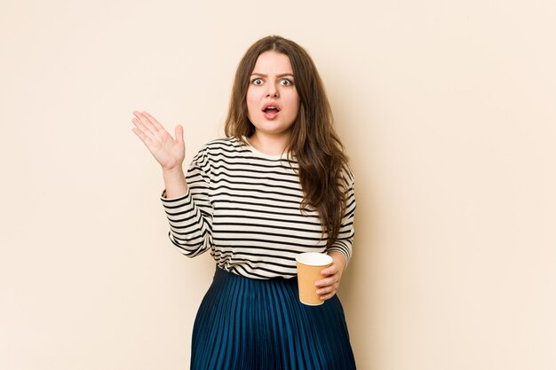 Jeune femme bien roulée tenant un café surpris et choqué