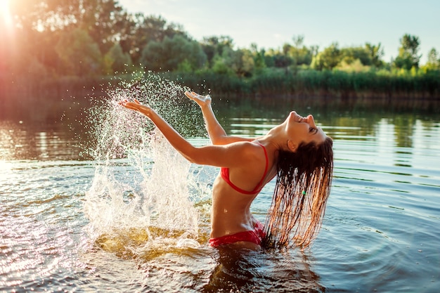 Jeune femme en bikini jouant dans l'eau de la rivière et faisant des éclaboussures