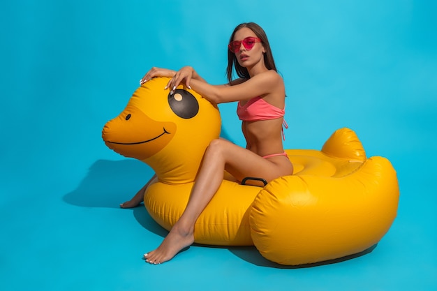 Jeune femme en bikini et lunettes de soleil assis sur un canard gonflable