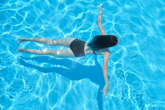 Jeune femme en bikini nageant sous l'eau dans une piscine extérieure, vue de dessus.