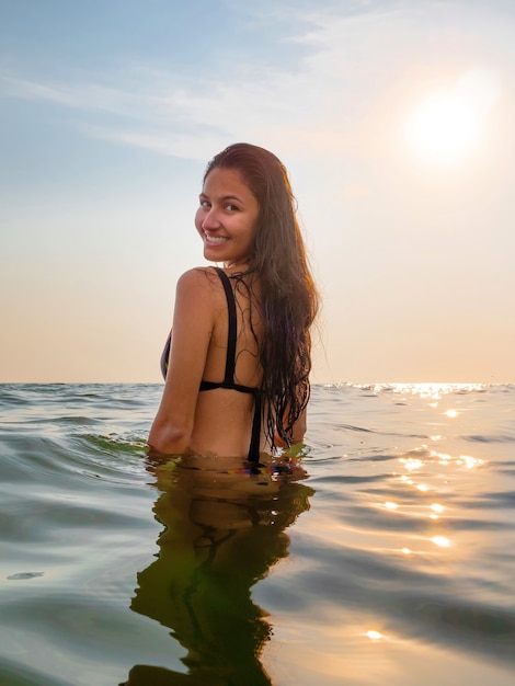 Jeune femme en bikini prend un bain dans la mer aux lumières du coucher du soleil en été.