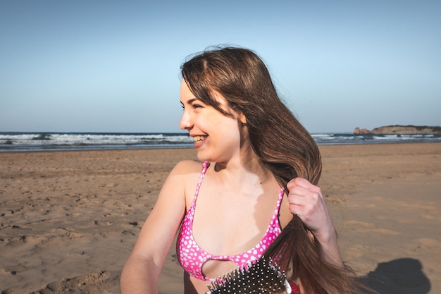 Jeune femme avec un bikini rose sur la plage se brosser les cheveux avec un peigne.