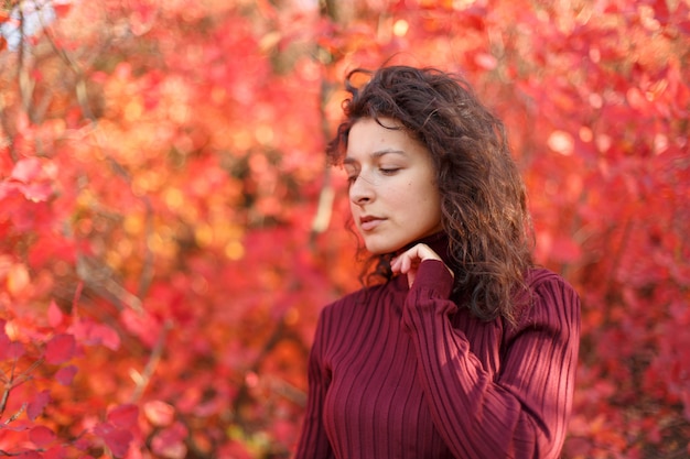 Jeune femme blackhaired en rouge sweather se présentant à la caméra dans les buissons de autumnn rouges.