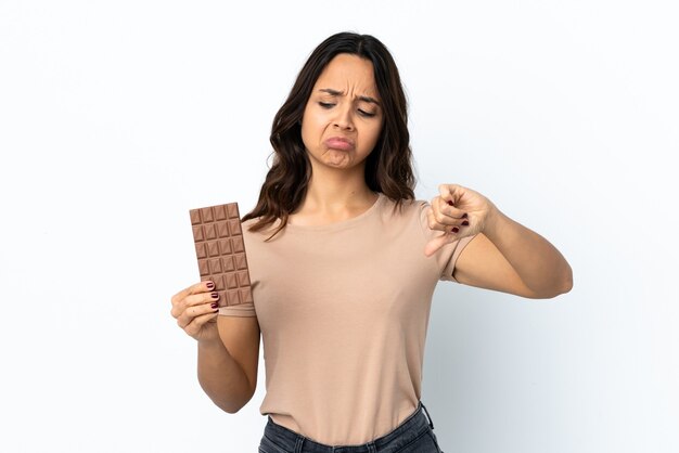 Jeune femme sur blanc isolé prenant une tablette de chocolat faisant un mauvais signal