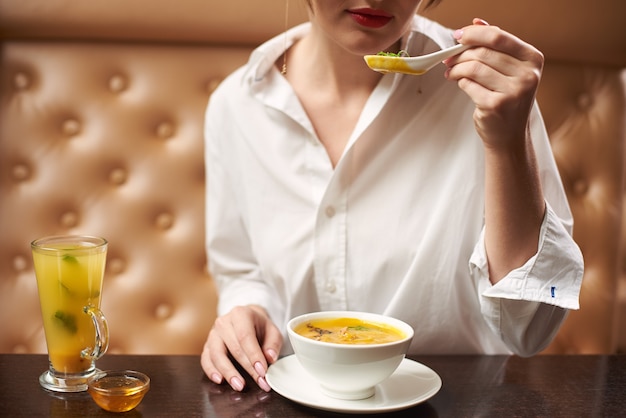 Jeune femme en blanc manger une soupe à la crème savoureuse.