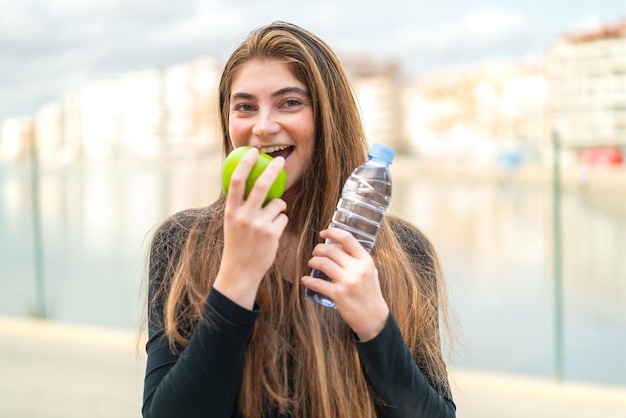 Une jeune femme blanche avec une bouteille d'eau et une pomme.