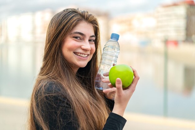 Une jeune femme blanche avec une pomme et une bouteille d'eau.