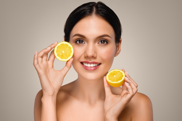 Une jeune femme blanche positive avec un visage parfait montre des citrons jaunes et des fruits