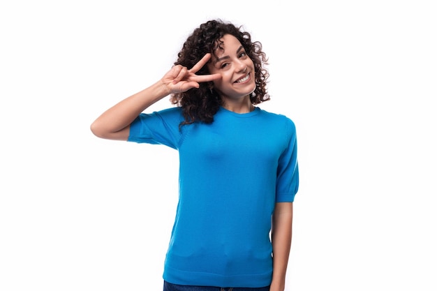 Une jeune femme blanche souriante et soignée avec des boucles est vêtue d'un t-shirt bleu.