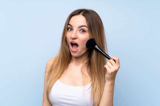 Jeune femme sur bleu isolé avec pinceau de maquillage